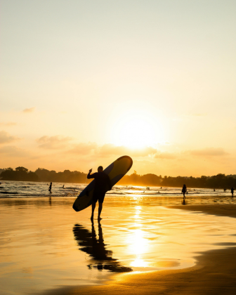 A surfer silhouetted against a golden sunset, carrying a board along Arugam Bay's shoreline.