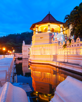 The Temple of the Tooth Relic illuminated at night, reflected in the still water of Kandy Lake.
