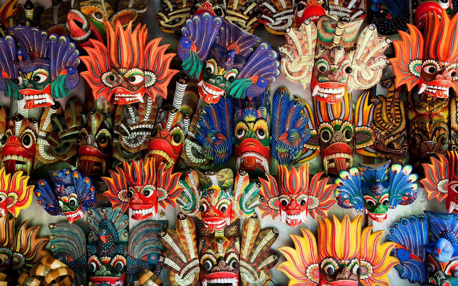 A dense wall of traditional hand-painted Sri Lankan devil and fire masks in vivid red, blue, and gold.