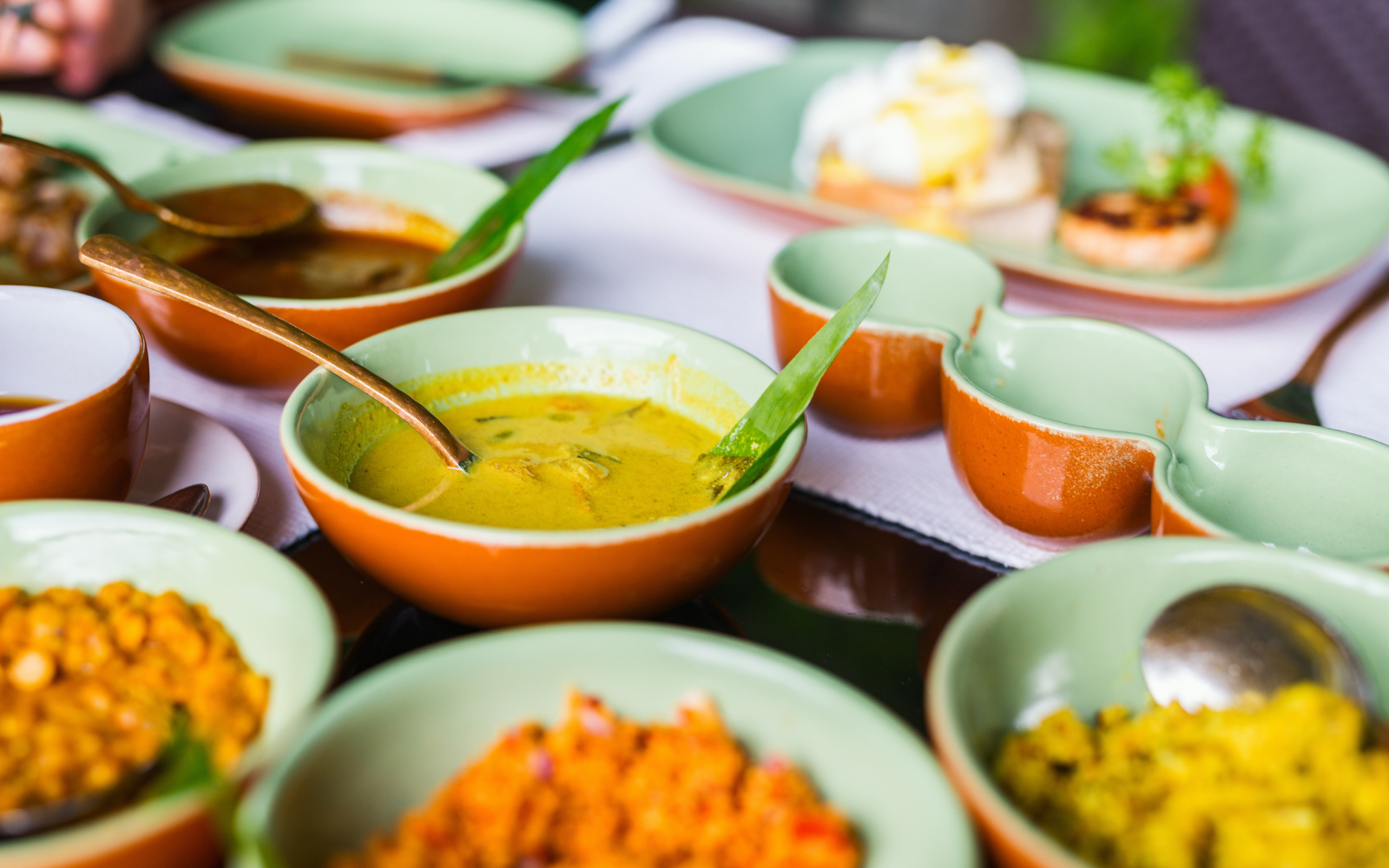A spread of Sri Lankan curries and sambols in ceramic bowls, garnished with pandan leaf.